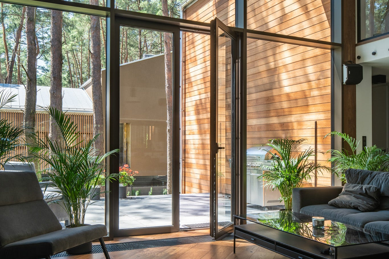 Modern living room with large glass doors leading to a patio, surrounded by trees.